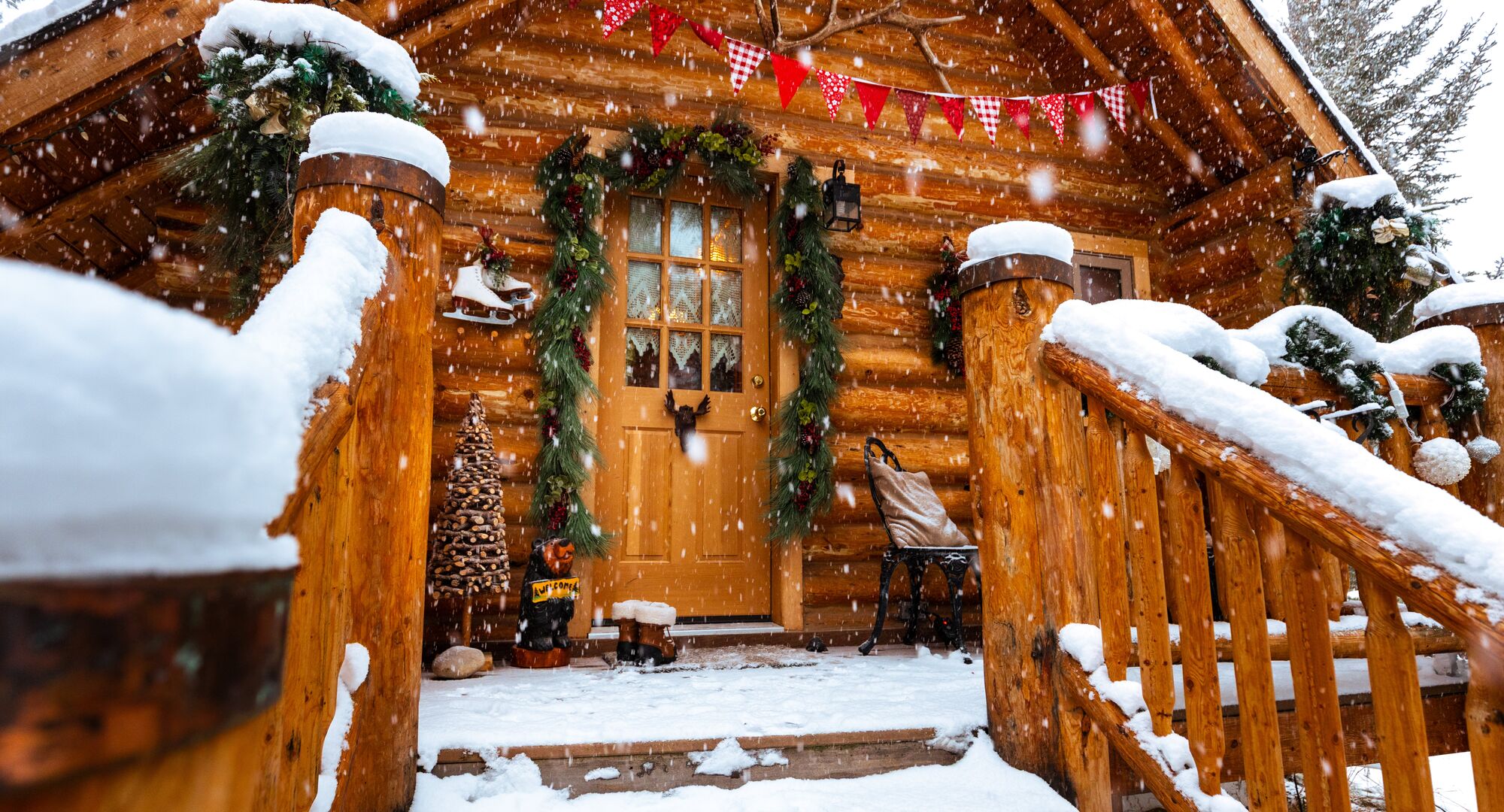 Snowy winter wood cabin with ice skates hanging outside with a welcome sign and Christmas decorations.